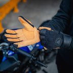 Person wearing brown and black gloves with a motorcycle in the background