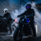 Two motorcyclists on their bikes in a dimly lit tunnel with smoke effects.