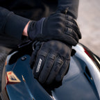 Person wearing black gloves touching a motorcycle helmet