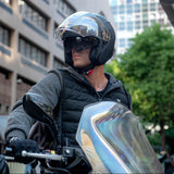 Person wearing a helmet and dark jacket on a motorcycle in an urban setting