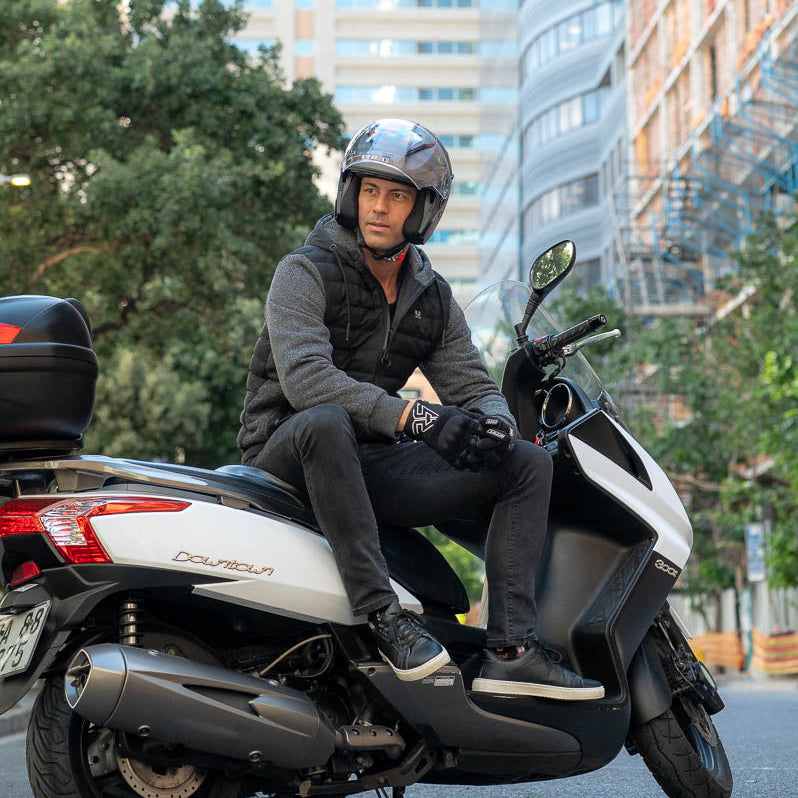 Man riding a scooter in an urban setting with tall buildings in the background